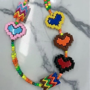 Collar de cuentas Y2K con colgantes de corazón pixelados sobre fondo de mármol blanco