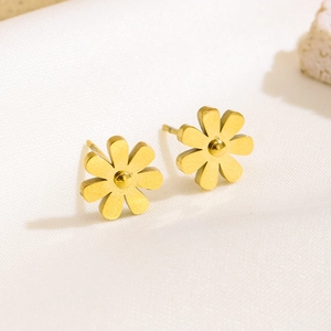 Close-up of matte gold daisy earrings with brushed metal finish on white silk