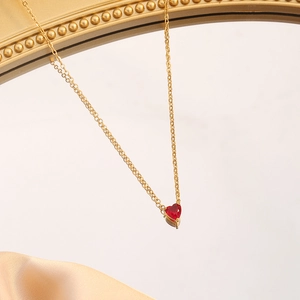 Golden stainless steel necklace featuring a red heart gemstone pendant on a mirror background
