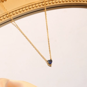Close-up of golden heart pendant necklace with blue gemstone on a gold mirror