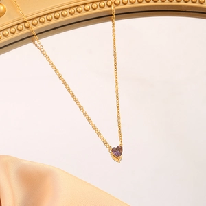 Macro detail of gold stainless steel heart pendant necklace with purple gemstone