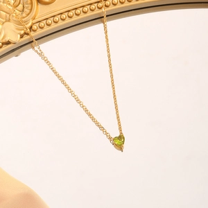Macro view of gold heart pendant necklace featuring a brilliant green May birthstone
