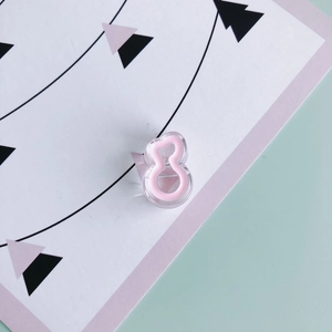 Close-up of a pink 8-shaped acrylic hair clip on a geometric illustration card