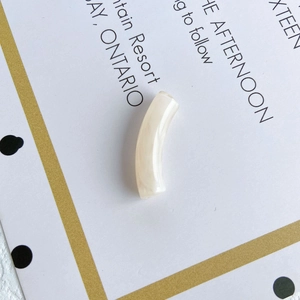 Close-up of a cream-colored curved tube bead with marble texture for DIY jewelry making