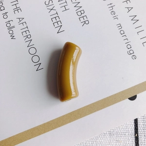 Close-up of mustard yellow resin curved tube bead with polished finish for jewelry making
