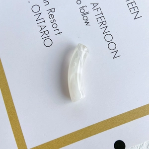 Macro view of a white translucent curved resin tube bead with marble texture