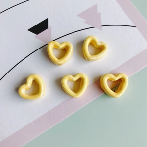 Nahaufnahme von fünf leuchtend gelben, hohlen herzförmigen Keramikperlen für DIY-Schmuck