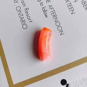 Gros plan d'une perle tube courbée en acrylique marbré orange et blanc pour bijoux DIY