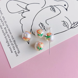 Close-up of four floral pearl beads with orange hearts and green leaves for DIY crafts