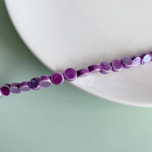 Macro shot of purple flat ceramic beads for DIY jewelry making on white porcelain plate