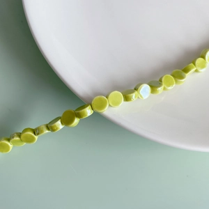 Detailed close-up of avocado green flat round ceramic beads for DIY jewelry making