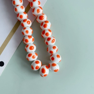 Dettaglio di perle in ceramica bianca con pois arancioni per gioielli fai-da-te
