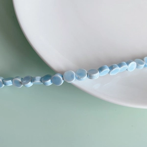 Detail of light blue flat round ceramic beads on a white porcelain plate with green background