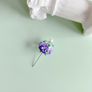 Detail of handcrafted glass charm pin with purple spiral patterns and silver metal needle