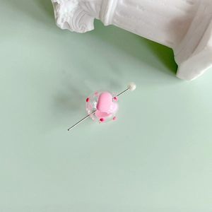 Close-up of hollow glass bead with red dots, pink heart and pearl on a metal jewelry pin