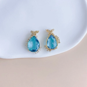 Detail of pear-shaped blue gemstone earrings with zircon-studded angel wing accents