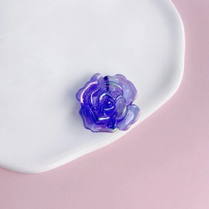Macro detail of a purple acrylic rose bead with aurora coating on a white ceramic tray