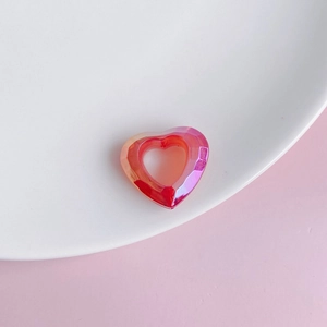 Macro detail of iridescent red-pink gradient resin heart pendant on white ceramic plate