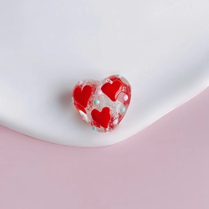 Macro detail of clear heart glass bead with red hearts and 3D colored polka dots