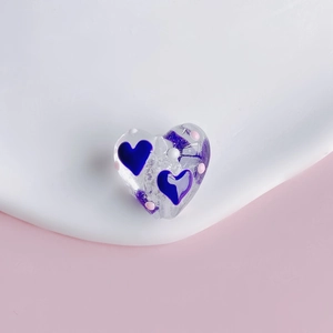 Macro shot of transparent heart-shaped bead with blue hearts and colorful dots for DIY