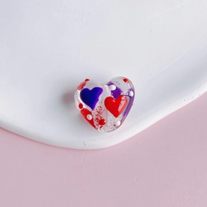 Macro detail of heart-shaped transparent beads with red hand-painted dots for DIY jewelry