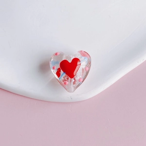 Macro detail of a transparent heart-shaped glass bead with red heart and arrow motifs