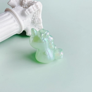 Macro shot of light green iridescent resin unicorn charm with pearl finish on white pedestal