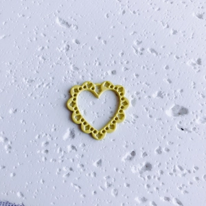 Detail of yellow heart-shaped pendant with hollow lace design for DIY jewelry making