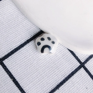 Close-up of a glossy ceramic cat paw pendant featuring a black and white hand-painted finish