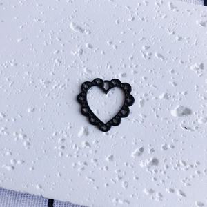 Macro detail of black openwork heart charm with scalloped edges for DIY jewelry making