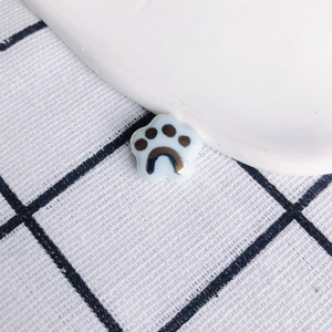 Detail of cute cat paw ceramic pendant charms on a black and white checkered fabric background
