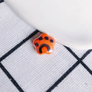 Detailed macro shot of orange glossy ceramic cat paw pendant with black paw prints