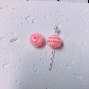 Detailed macro of pink and white striped acrylic candy beads on a pearlized metal pin