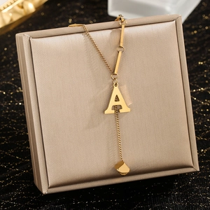 Detail of gold stainless steel Y-shaped necklace with letter A pendant and small cube tassel