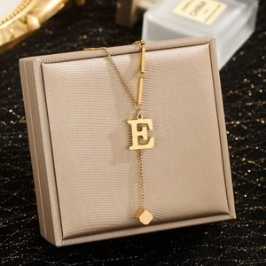 Detail of gold-plated stainless steel letter E pendant with dangling small cube charm
