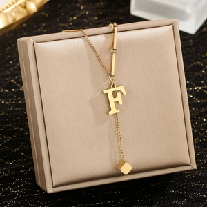 Detail of gold letter F pendant necklace with square tassel on a brushed display box