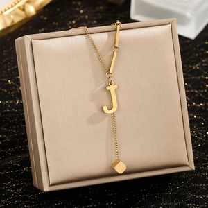 Detail of gold necklace with letter J pendant and cube tassel on jewelry box