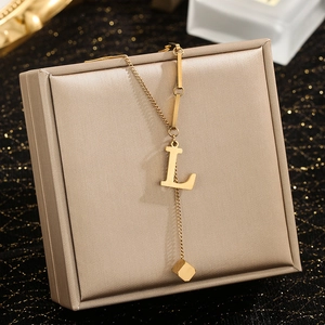 Detail of gold letter L pendant necklace with small cube charm on jewelry box