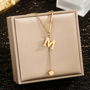 Detailed close-up of golden letter M pendant necklace on premium jewelry display box