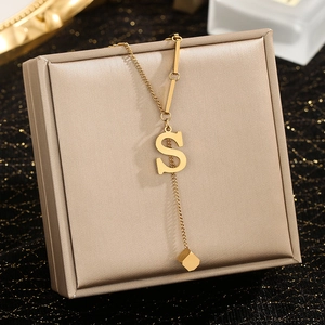 Macro detail of gold Y-shaped necklace featuring an S letter charm and cube pendant