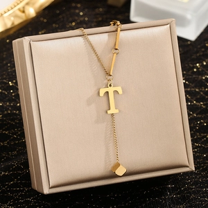Close-up of gold T-letter pendant necklace with square tassel drop on jewelry gift box