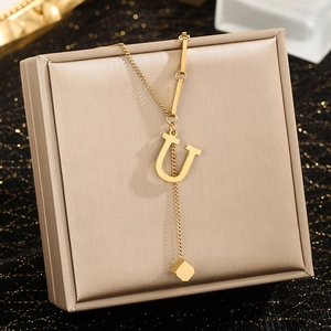 Close-up of golden letter U pendant necklace with square tassel on jewelry box