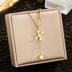 Detail of gold letter X pendant necklace with geometric chain on luxury gift box