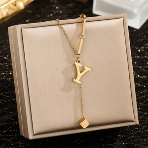 Macro detail of golden letter Y pendant with square charm and fringe chain on display box