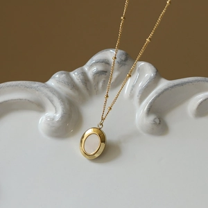 Detail of a vintage gold beaded necklace featuring an oval pendant with white inlay