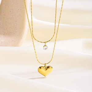 Elegante collar de doble capa dorado con corazón y circón sobre fondo de seda blanca