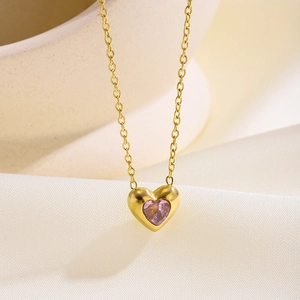 Detalle macro del collar dorado con colgante de corazón en circón rosa sobre seda suave