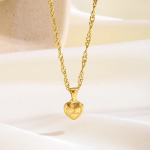 Primer plano de collar con colgante de corazón dorado y grabado Love sobre seda blanca