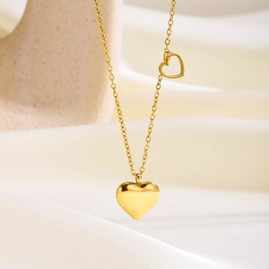 Detalle de collar de corazón dorado con pequeño corazón hueco sobre seda suave