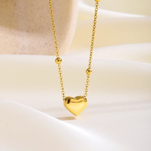 Primer plano del collar con colgante de corazón dorado sobre seda con cadena de cuentas